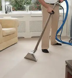Professional carpet cleaner using a hot-water extraction wand and hose machine in a living room in Saint Louis, MO.