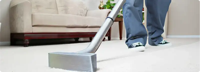 Carpet cleaning technician using a hot-water extraction wand on a light-colored carpet in a living room, Saint Louis, MO.