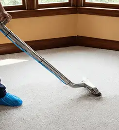 Steam carpet cleaning technician using a hot-water extraction wand on a residential carpet, wearing blue protective shoe covers Saint Louis, MO.