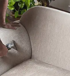 Professional upholstery cleaner deep-cleaning a fabric sofa with a handheld extraction tool and hose Saint Louis, MO.