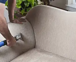Professional upholstery cleaner deep-cleaning a fabric sofa with a handheld extraction tool and hose in Saint Louis, MO.